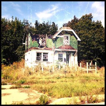 An old house with a green roof and overgrown yard.