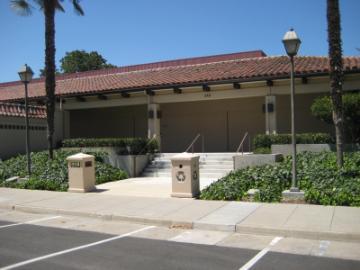 The entrance of Daly Science 100 building with greenery and palm trees.