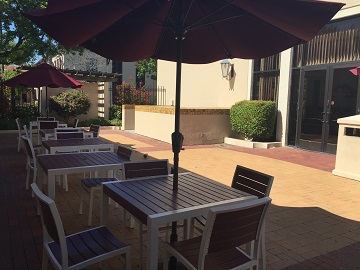 Outdoor patio with tables, chairs, and umbrellas under sunlight titled 'Shapell Patio'.