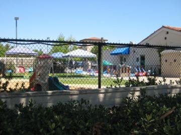 Outdoor play area with playground equipment and canopies, surrounded by buildings.