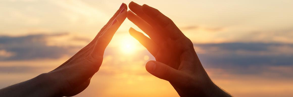 Two hands forming a triangle around the setting sun.