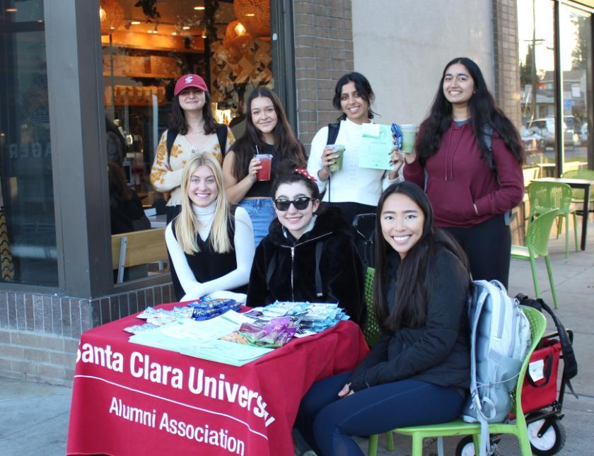 Group of students and young alumni huddled around red Student Alumni Council table