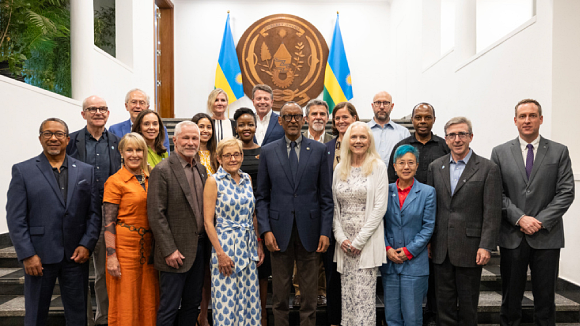 A group of smiling people, including Santa Clara University President Julie Sullivan and Rwandan President Paul Kagame, standing in front of a wall with the Rwandan seal.