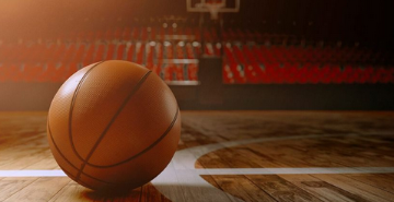 A basketball on an indoor court with a basket in the background. 