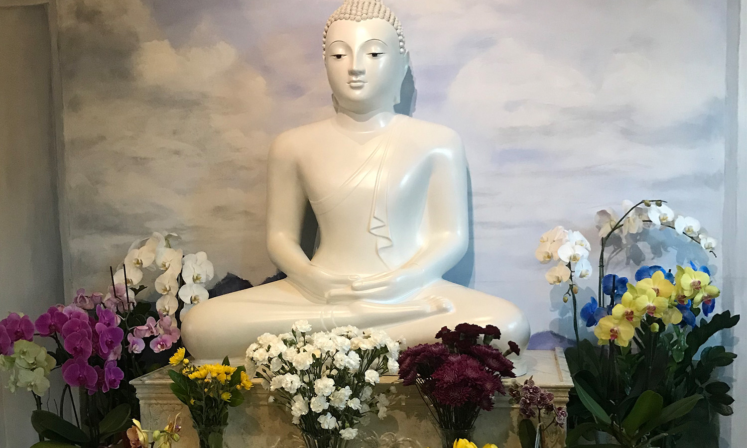 Buddhist statue surrounded by various colorful flowers.