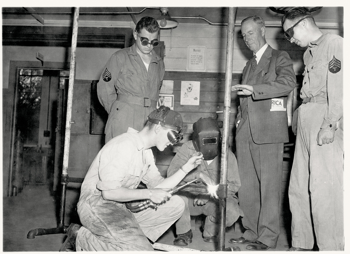 Four men inspecting machinery components in a mechanical workshop in 1943.