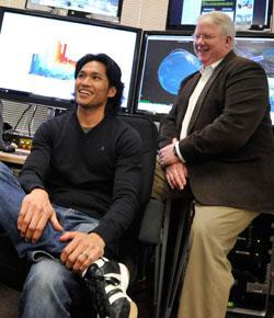 Two people discussing in front of multiple screens in a work setting.