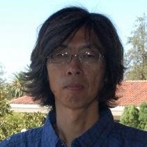 A person standing outdoors with trees and buildings in the background.