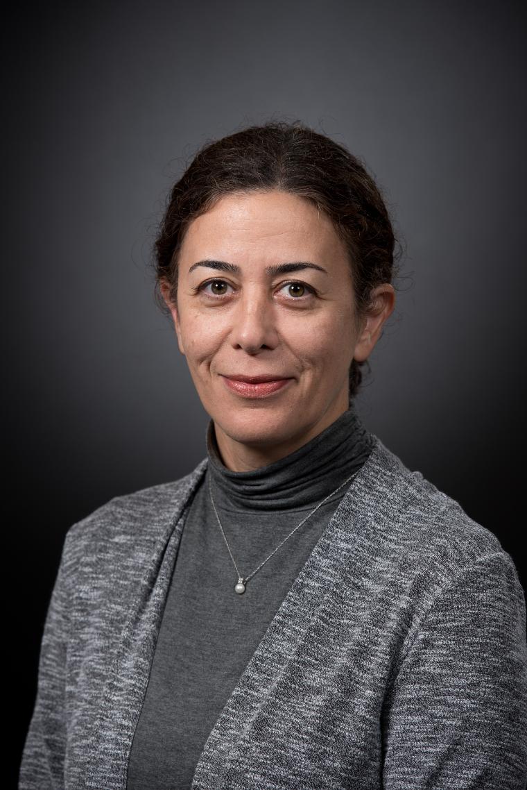 A person in a grey blazer against a dark background.