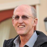 A man smiling outdoors wearing glasses and a jacket.