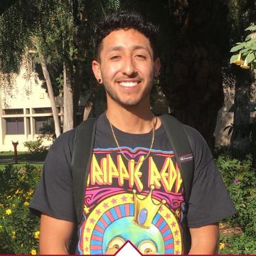 A person smiling outdoors with trees and buildings in the background.