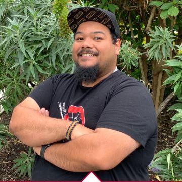 A person with crossed arms standing in front of greenery.