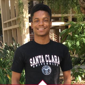 Young man in a Santa Clara University t-shirt smiling in an outdoor setting.