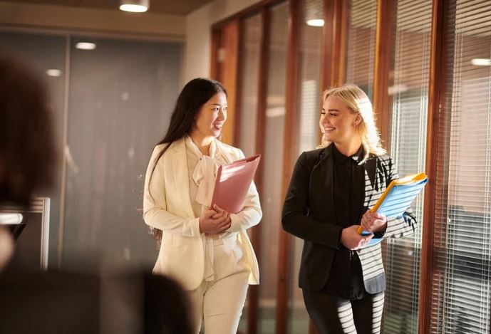 stock image of two young women one with brown hair one with blonde hair walking in a law office carrying files 
