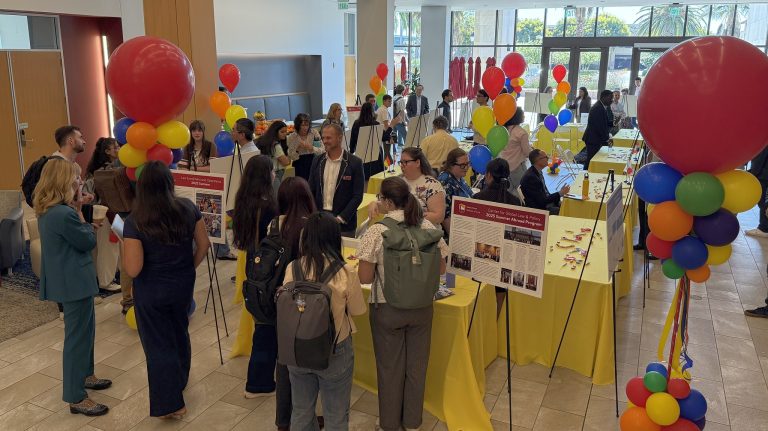 photo of the 2025 What I Did Last Summer event with tables, balloons, students and faculty members and posters of faculty scholarship activities image link to story
